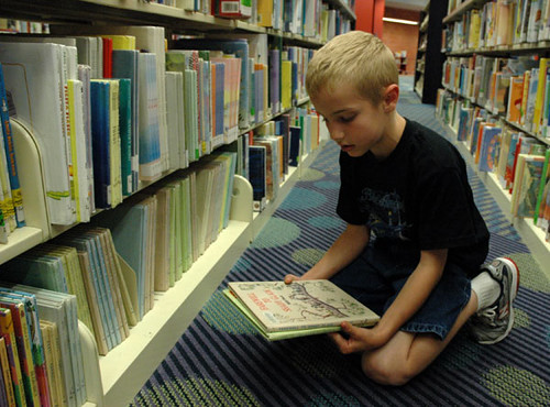 Image of a small boy reading a book on the floor of a library.