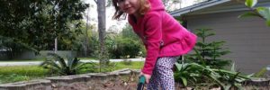 Image of a small girl shoveling dirt in a garden.