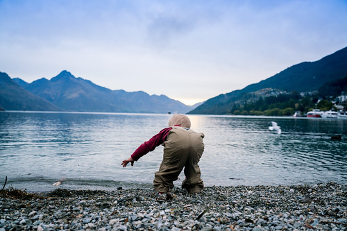 Young boy at the edge of a beutiful natural lake surrounded by mountains.