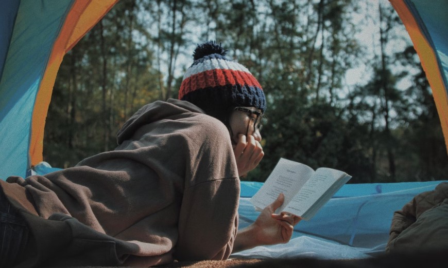 Girl laying down in a tent reading a book.