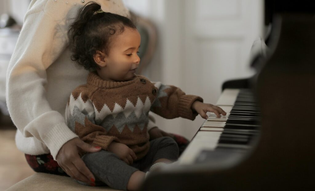 A child in a brown sweater on an adult's lap playing piano in Glenview, IL