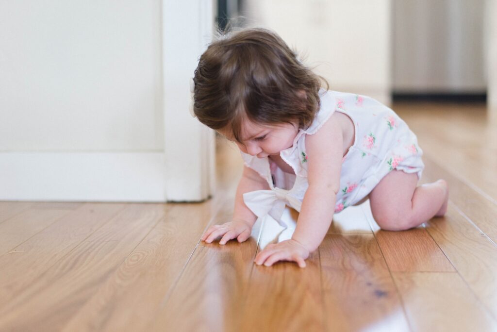 A young toddler crawling across a wooden floor.