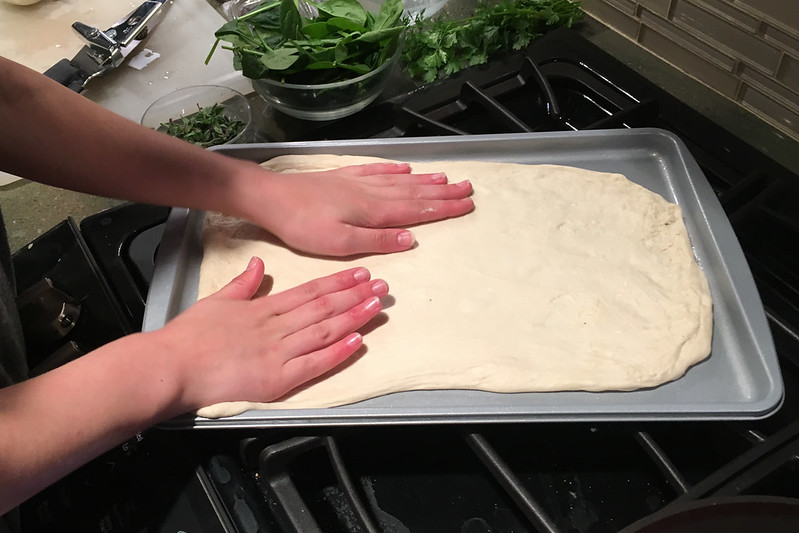 A child spreading out pizza dough onto a baking sheet in Lone Tree, CO