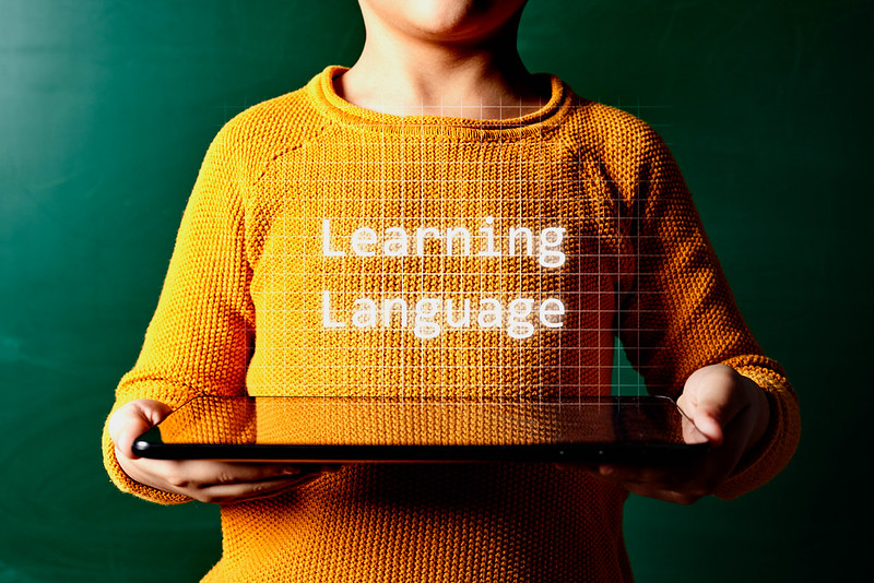 A child holding a tablet face up with the words "Learning Language" displayed above.