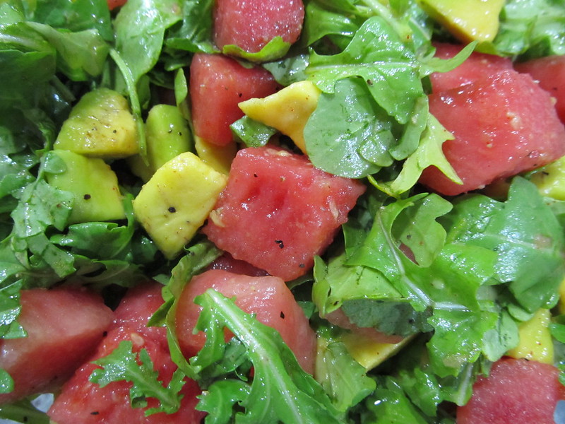 A close up photo of a fresh salad with watermelon, avocado, and arugula.