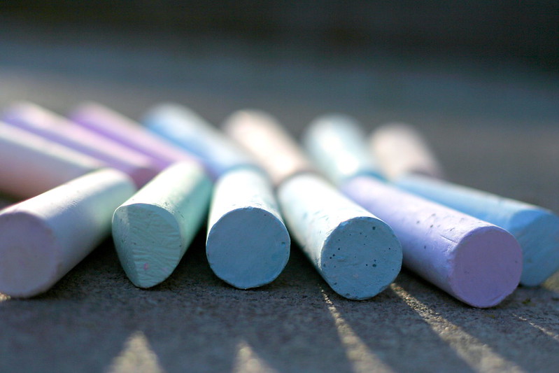 A lineup of colorful sidewalk chalk on a road.