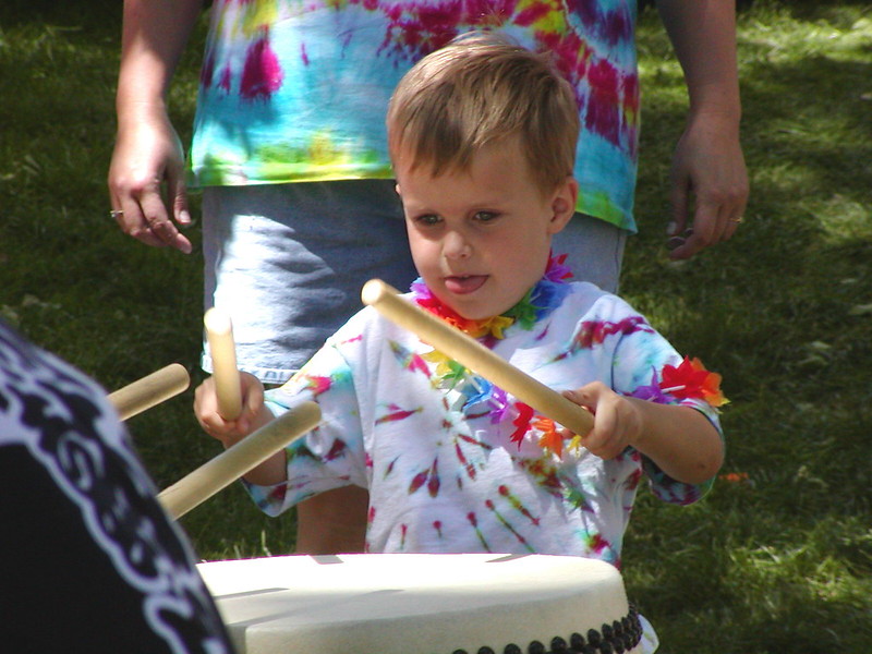 A small child in a tie-dye shirt hitting a drum with drumsticks