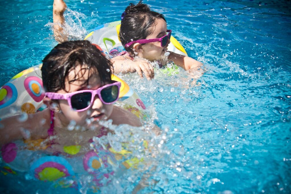Two small girls in sunglasses enjoying a pool with inner tubes.