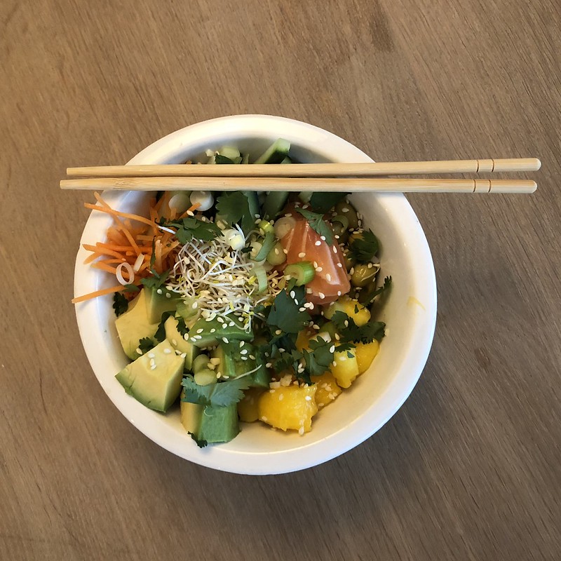 A poke bowl containing salmon and avocado with chopsticks.