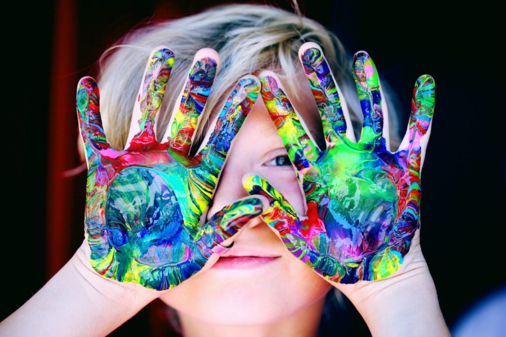 A child holding up his multi-colored paint covered hands.