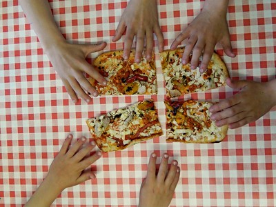 A pizza cut into four pieces with kids hands holding them on a checkered tablecloth