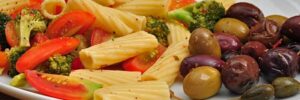 A plate of olives, pasta, and vegetables on a wooden table