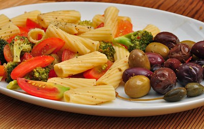 A plate of olives, pasta, and vegetables on a wooden table