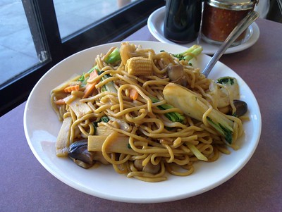 A Plate of vegetable Chow Mein on a table next to spices
