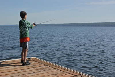A Young boy fishing out on a pier surrounded by a big blue body of water
