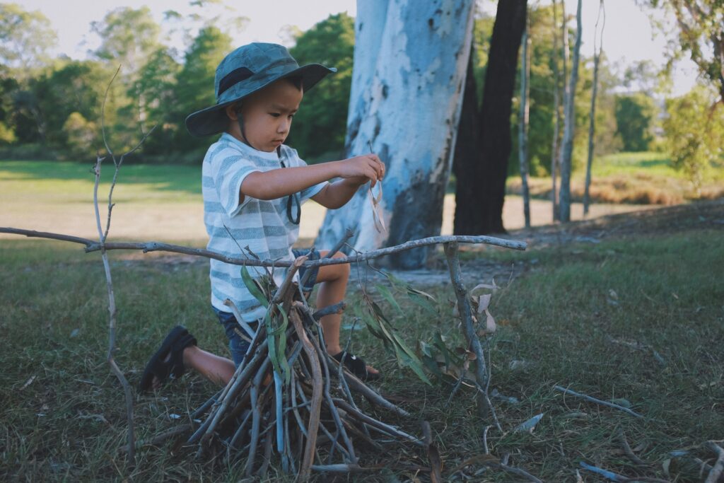 A little boy in the woods wearing a bucket hat making a fire