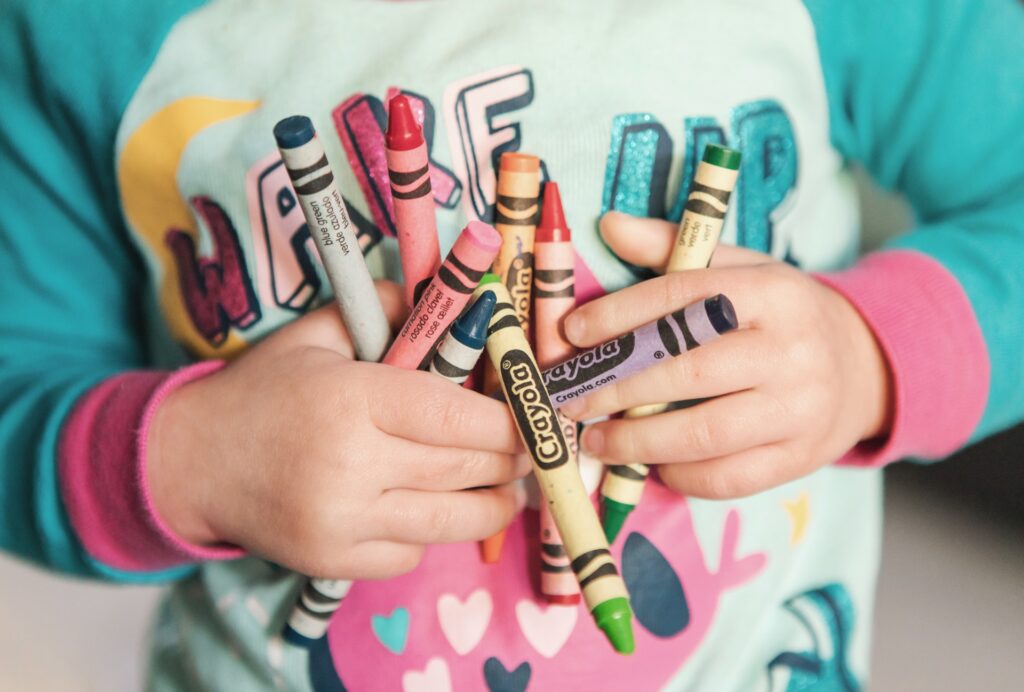 A child holding a colorful array of crayola crayons.