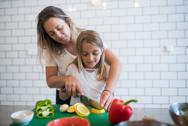 Mom in White Tank Top Assisting Daughter to Chop Lemon