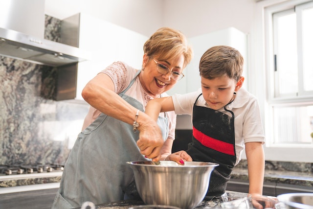 A young Boy and his grandma in the kitchen mixing ingredients in a silver bowl together