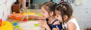 Two little girls making shapes out of flour in the kitchen.