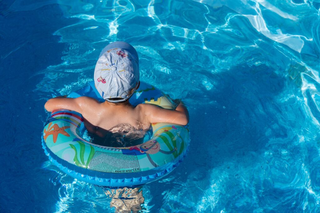 A child in a hat, floating with an innertube in a pool in Indiana.