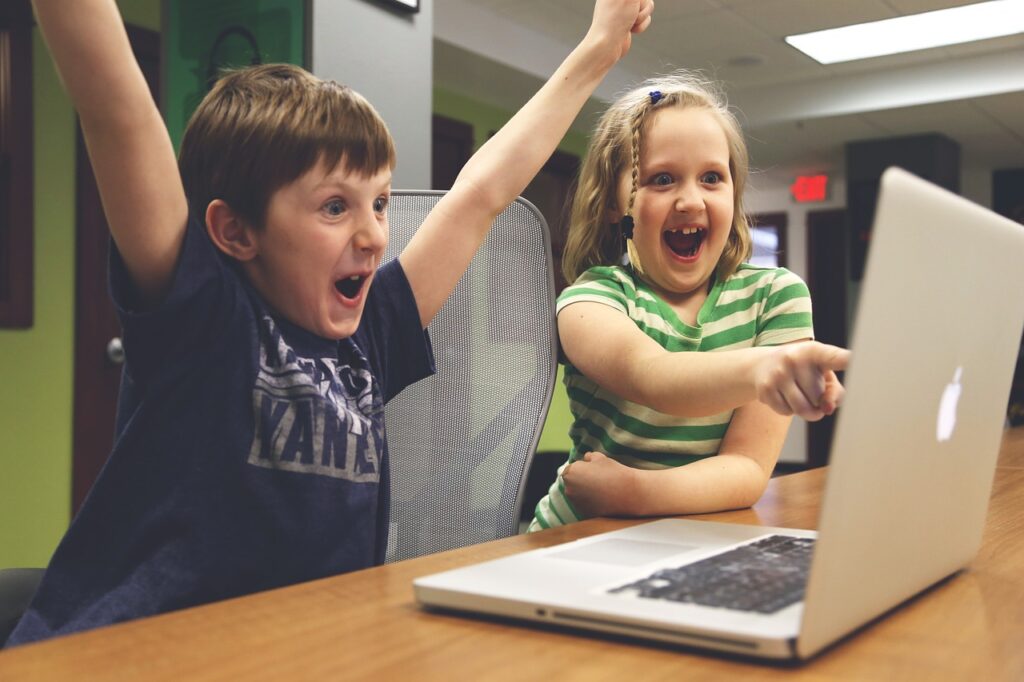 Two children excited to learn how to code on a laptop in a school