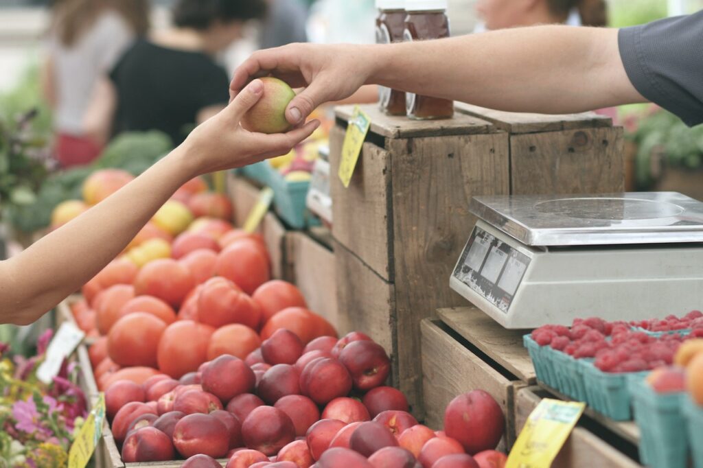 A vendor giving an apple to a customer at a farmers market in Texas.