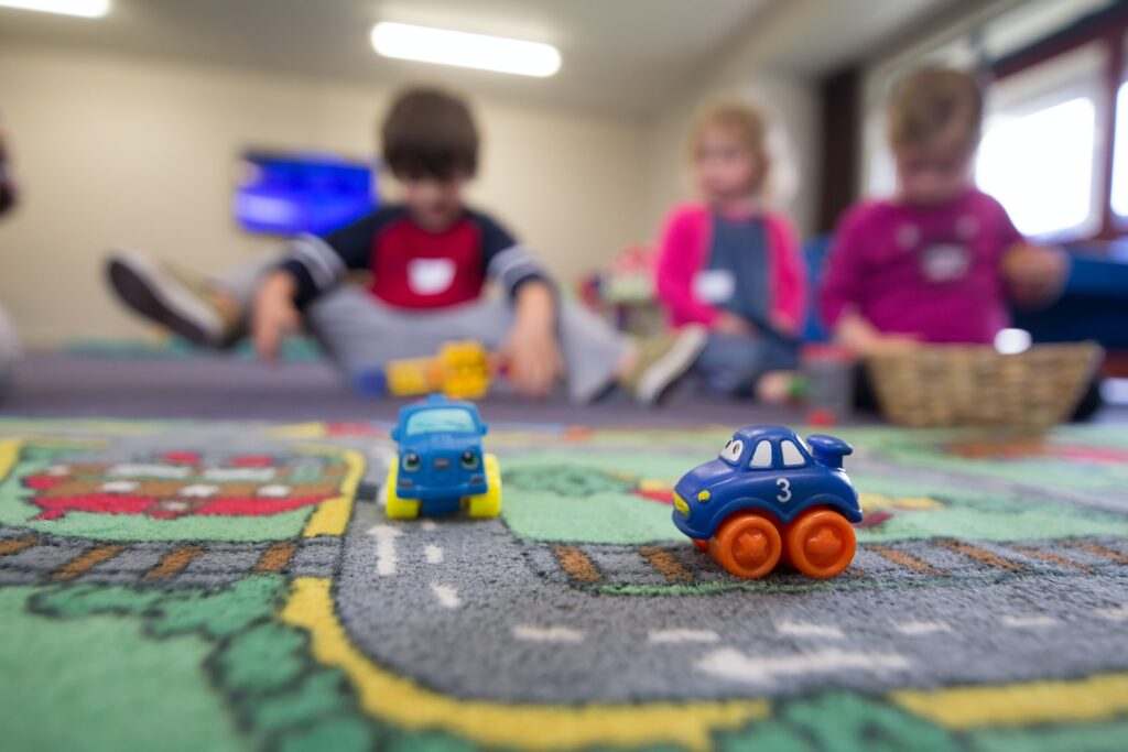 3 children playing on a rug with toy cars at a daycare.