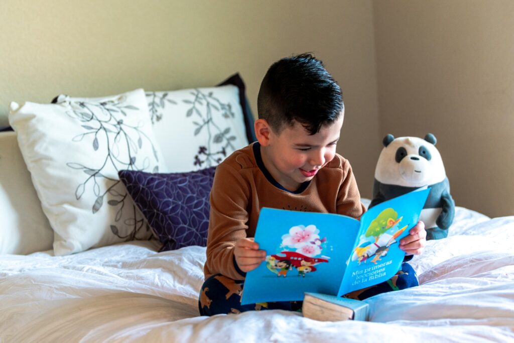 A child with a panda stuffed animal reading a book in bed.