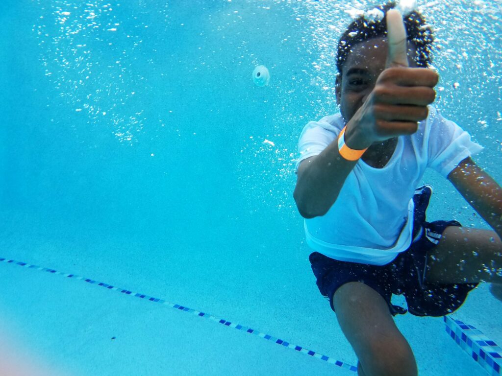 A young child giving a thumbs up while underwater in a pool in Chandler, AZ