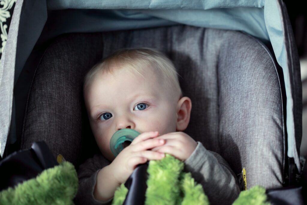 A child with a pacifier in a grey car seat.