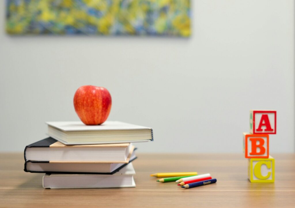 An apple sitting atop a stack of books and some blocks on a desk in Plano, TX
