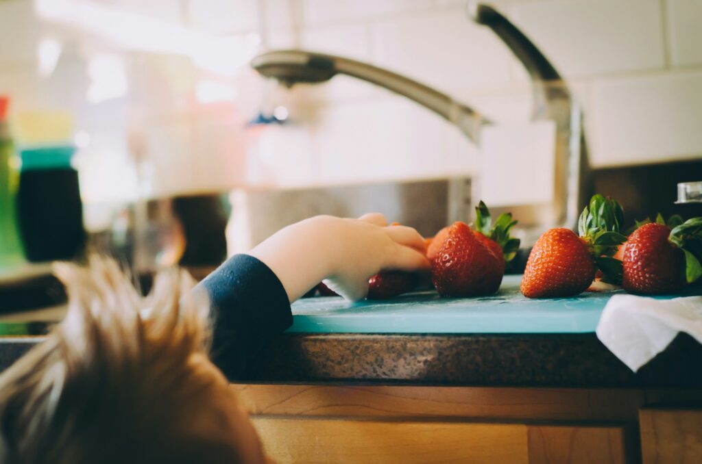 A child reaching up to a sink to grab strawberries.