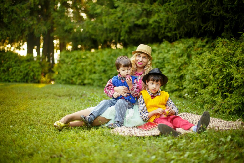 Two Boys Sitting in Front of Woman on Green Grass Field