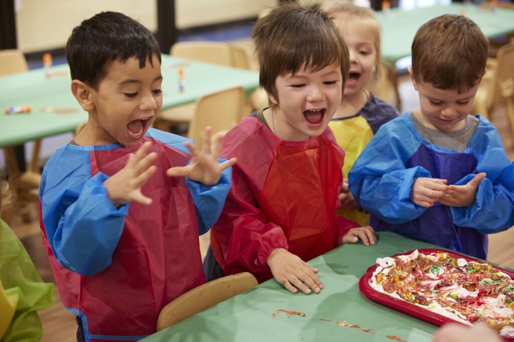 Kids smiling and laughing at a table with arts supplies and paint