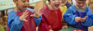 Kids smiling and laughing at a table with arts supplies and paint