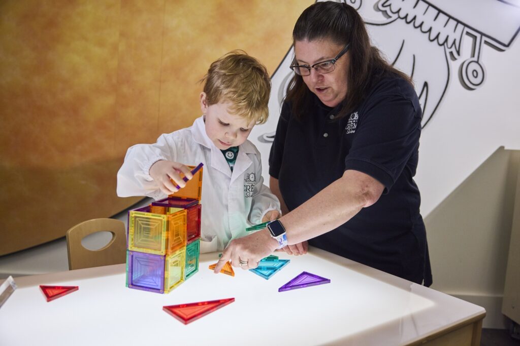 Child in lab coat with teacher doing experiment.