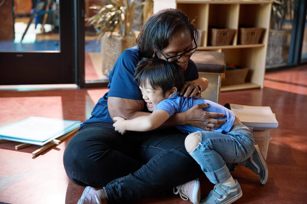 Teacher and child happily hugging in a class