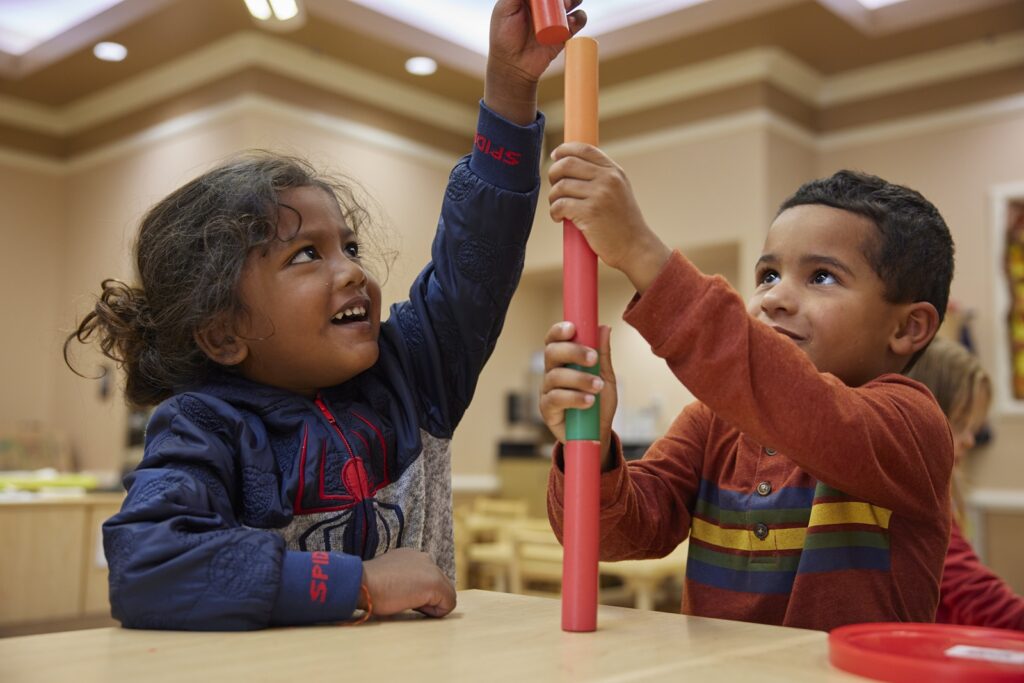 Two children in a classroom stacking objects