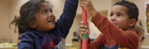 Two children in a classroom stacking objects