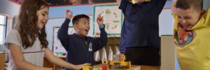 3 children at a table playing a game and cheering with teacher