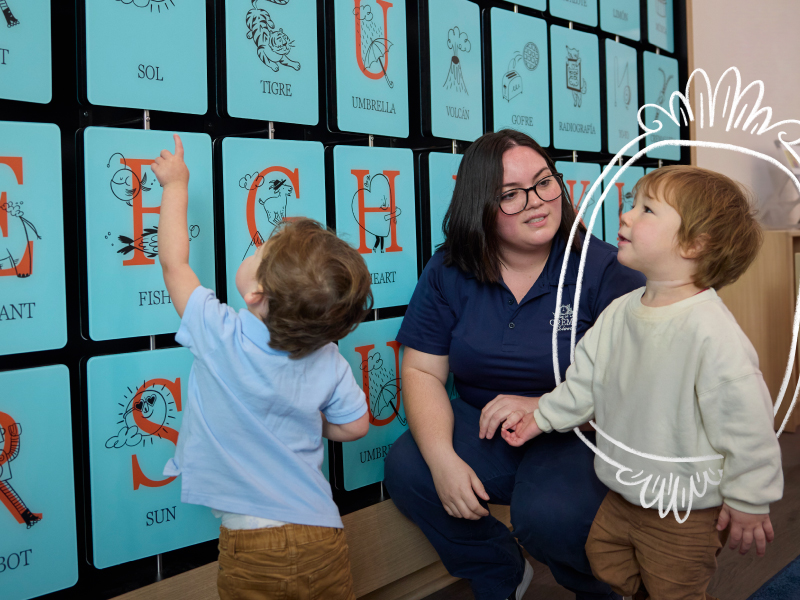 A young toddler in a blue sweater, playing with clear green and yellow blocks during an early childhood education class.