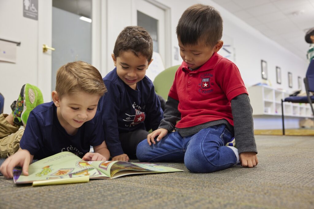 Three children sitting on the floor reading a book.