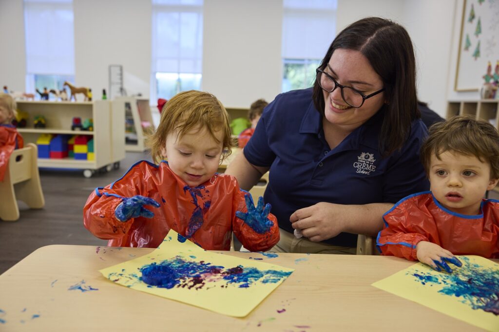 Two preschoolers finger painting with teacher watching
