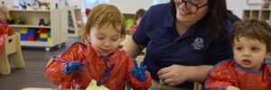 Two preschoolers finger painting with teacher watching